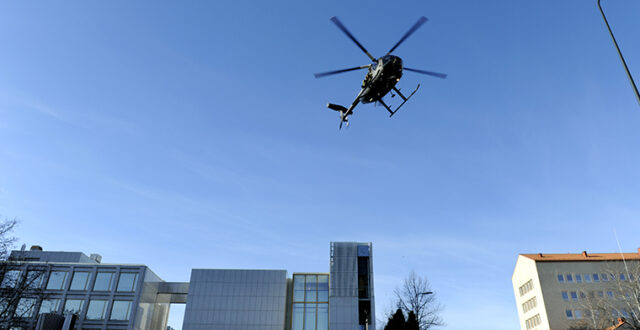 NH90 helikopteri lentää Kouvolan kaupungintalon yläpuolella sinistä taivasta vasten.